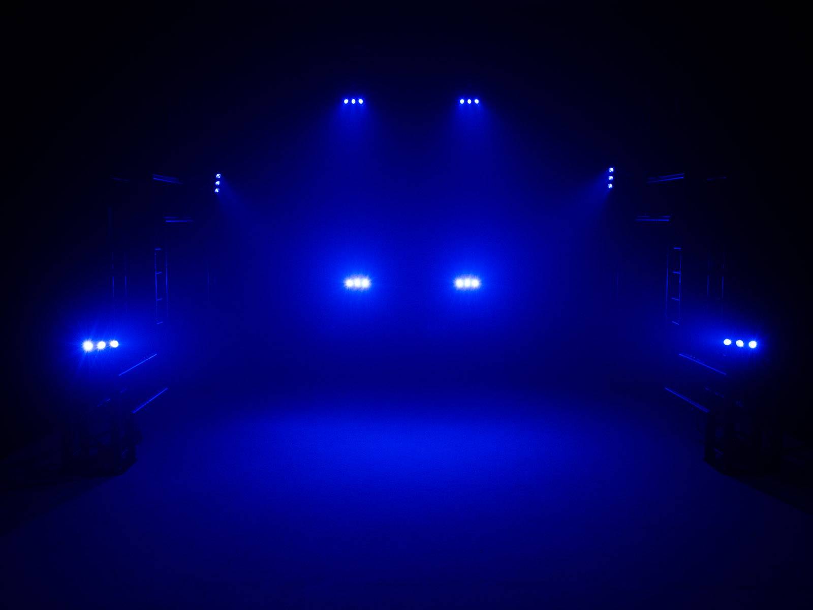 Niebieskie światła sceniczne oświetlają ciemną przestrzeń, koncentrując się na środku, tworząc mistyczną i ekscytującą atmosferę.