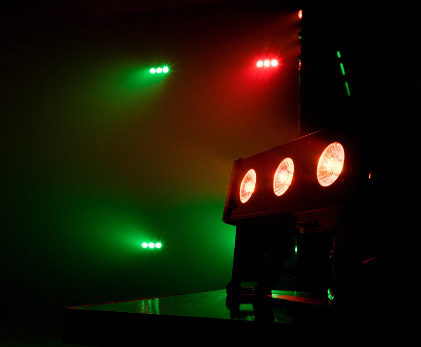 Trzy czerwone reflektory oświetlają scenę, po lewej stronie widać zielone punkty świetlne. Nastrojowo i kolorowo.
