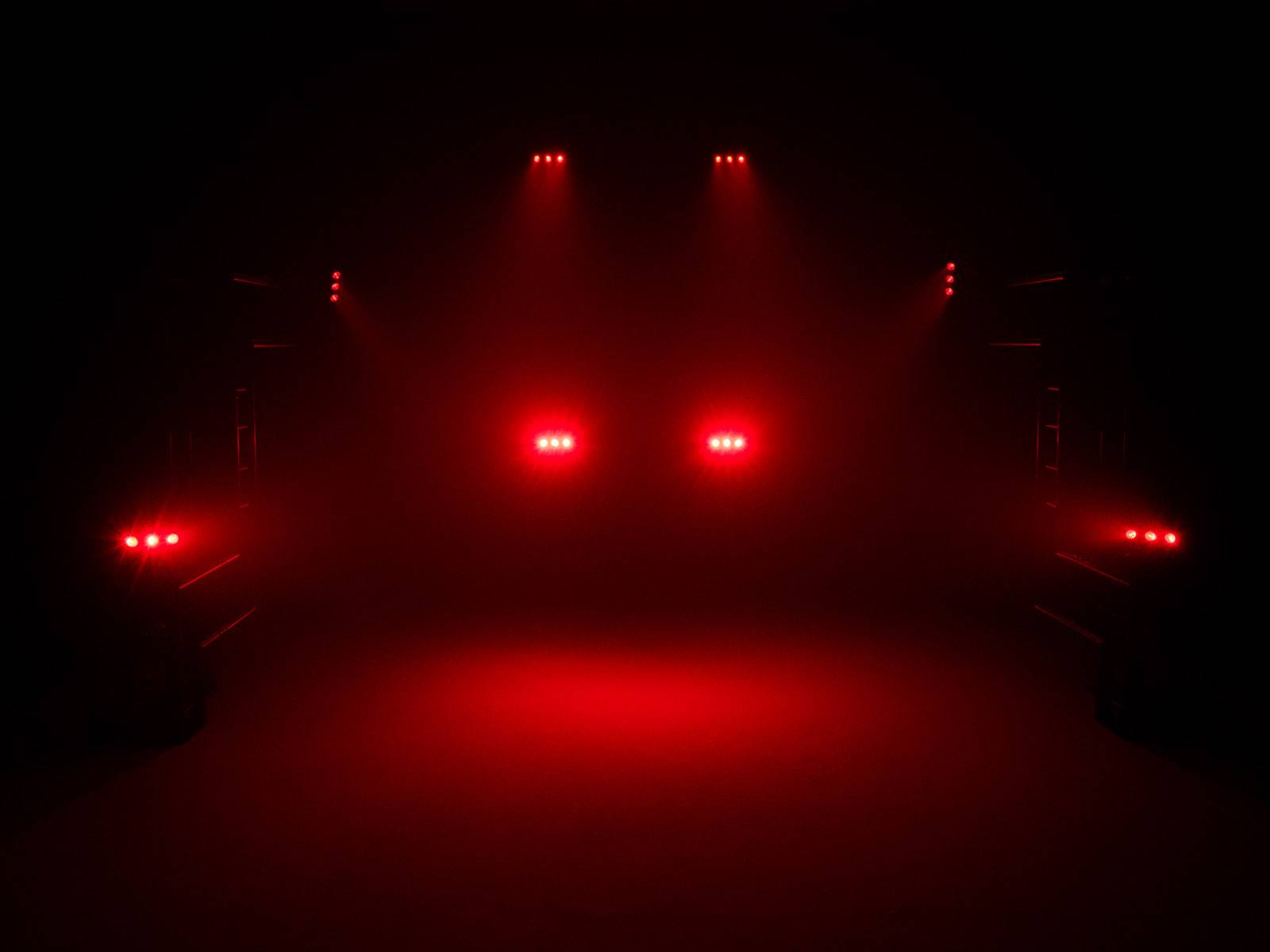 Czerwone światła świecą w ciemnym pokoju, przypominając tło sceniczne.