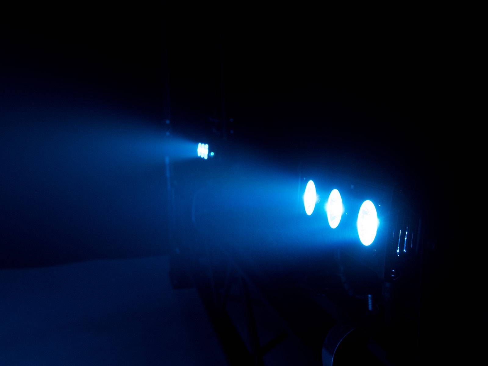 Niebieskie reflektory rzucają stożek światła w ciemnym pomieszczeniu, tworząc atmosferę futurystyczną.