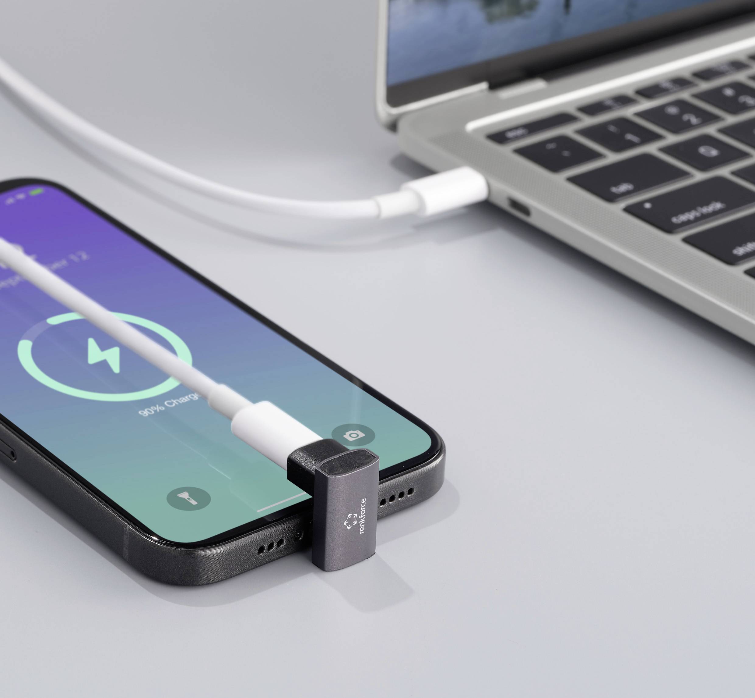 Smartfon ładuje się obok laptopa. Kabel ładujący jest podłączony, a ekran wyświetla 54% poziomu naładowania baterii.