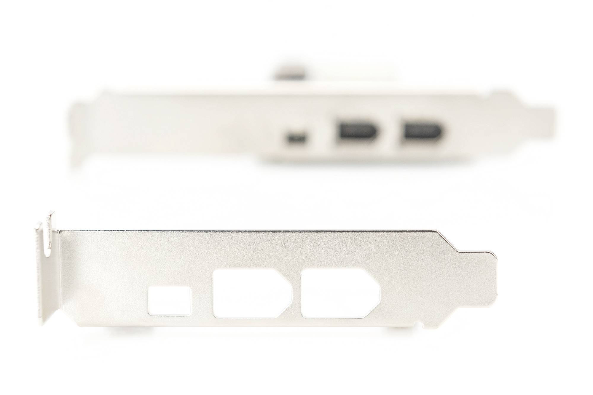 Dwie srebrne zaślepki komputerowe w rozmyciu. Ostrość pierwszoplanowa na wyciśniętej blasze z otworami, tło z portami USB.