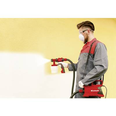 Mężczyzna rozpyla żółtą farbę na ścianę za pomocą pistoletu natryskowego. Jest ubrany w maskę ochronną, okulary ochronne i odzież roboczą.
