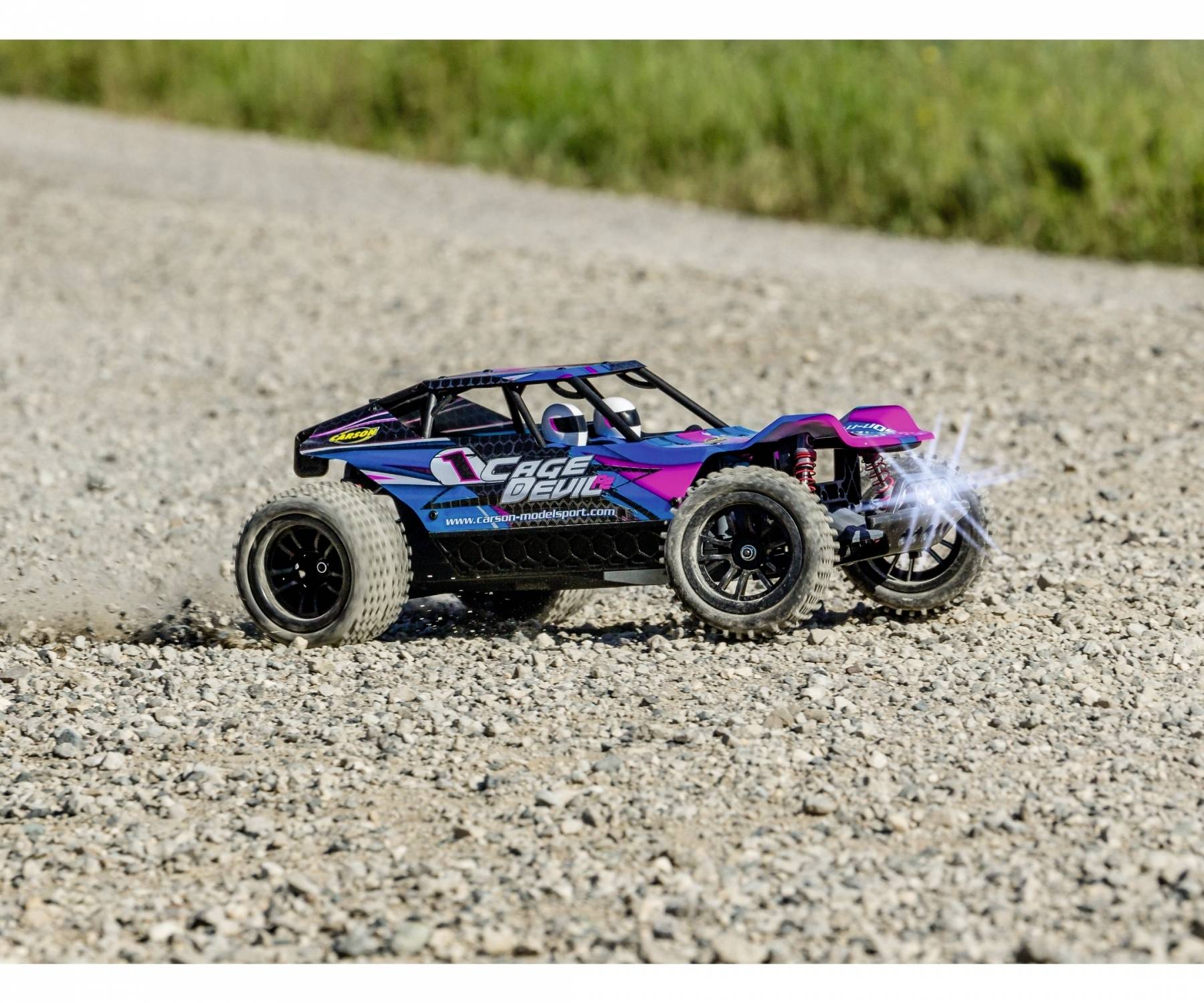 Zdalnie sterowany samochód szybko jedzie po drodze żwirowej, wywołując kłęby kurzu. Wyraziste kolory: niebieski, różowy, czarny.