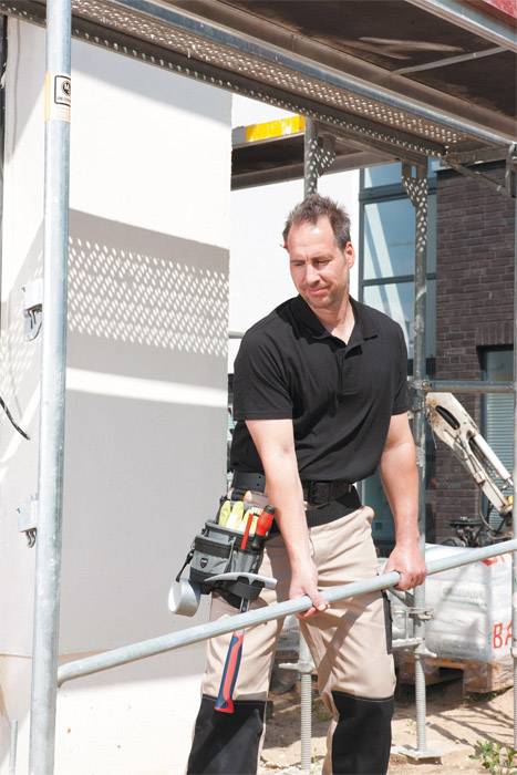 Robotnik budowlany podnosi stalowy element na placu budowy, otoczony rusztowaniami i sprzętem budowlanym.