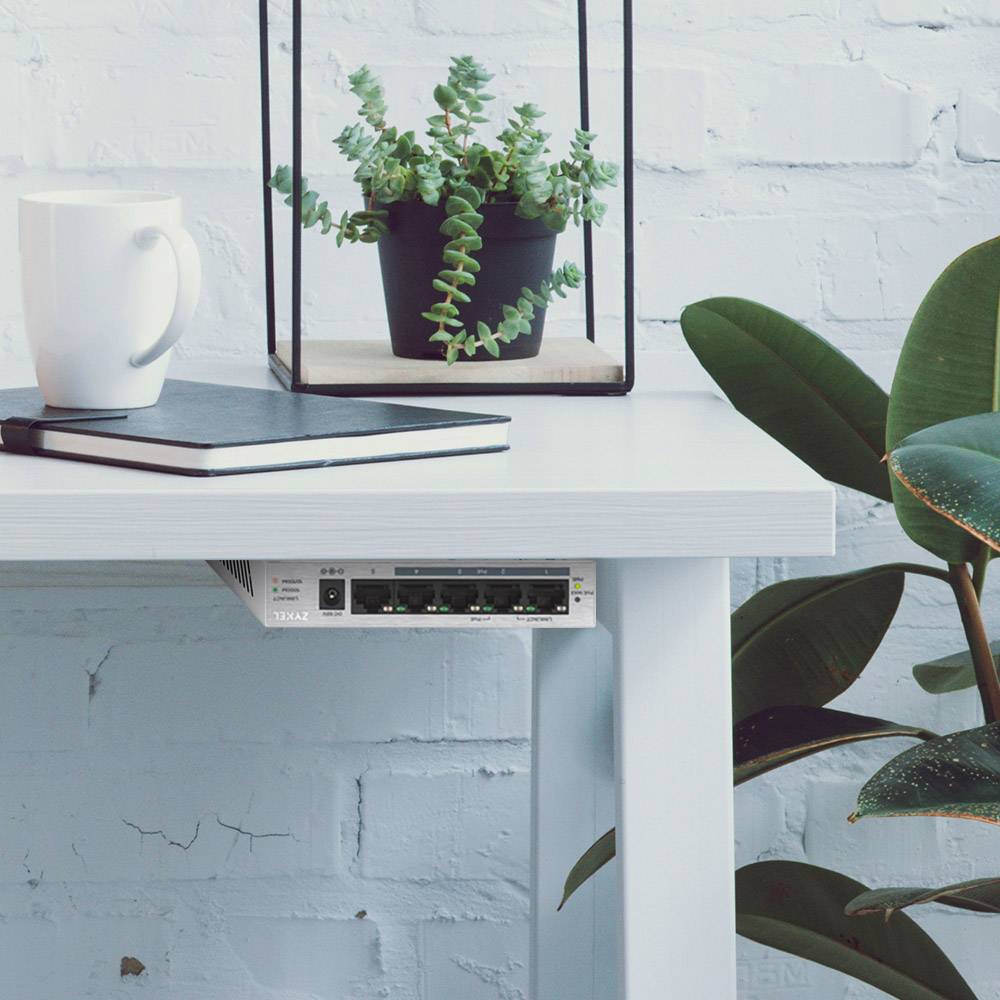 Biały stół z filiżanką, notatnikiem i doniczką z sukulentami. Poniżej przy krawędzi stołu zamontowane jest urządzenie sieciowe.