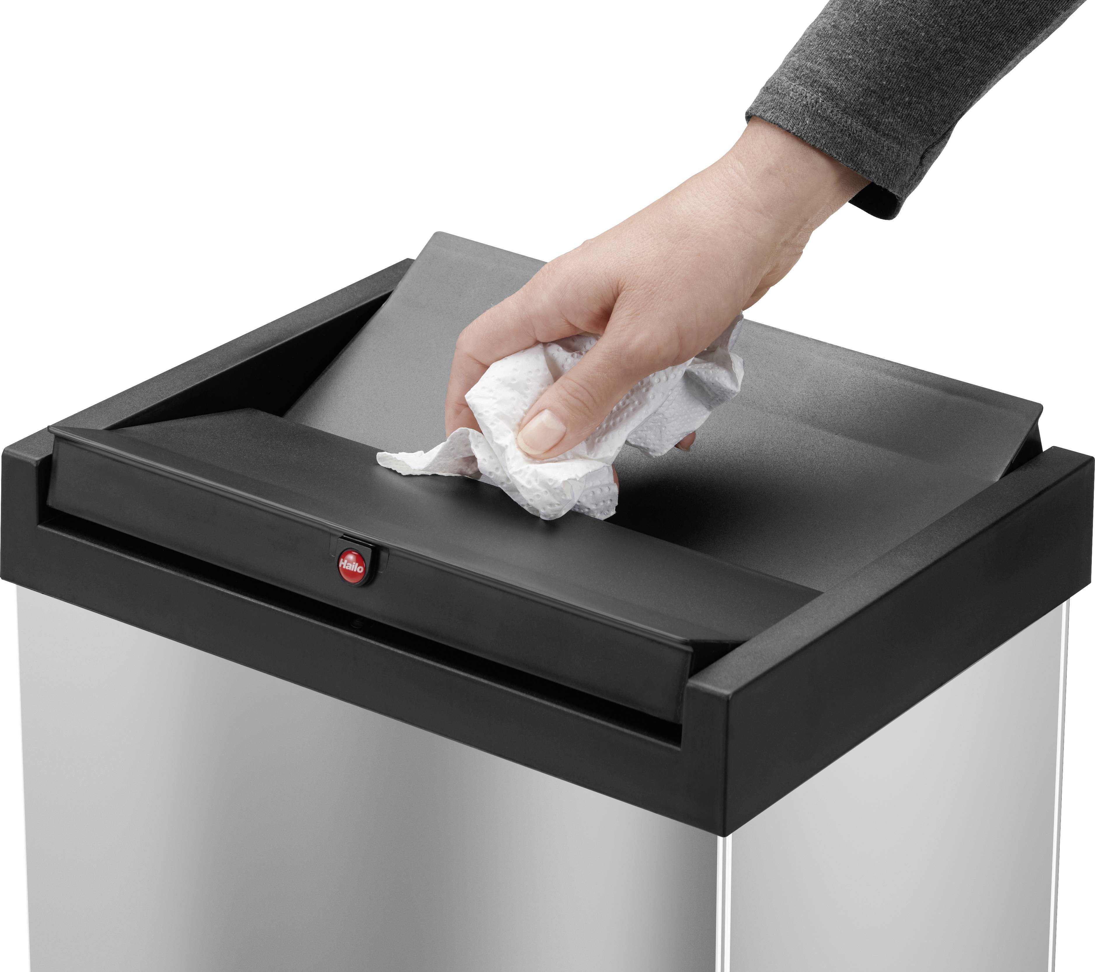 Dłoń wrzuca zmiętą chusteczkę do srebrnego kosza na śmieci z czarną pokrywką.