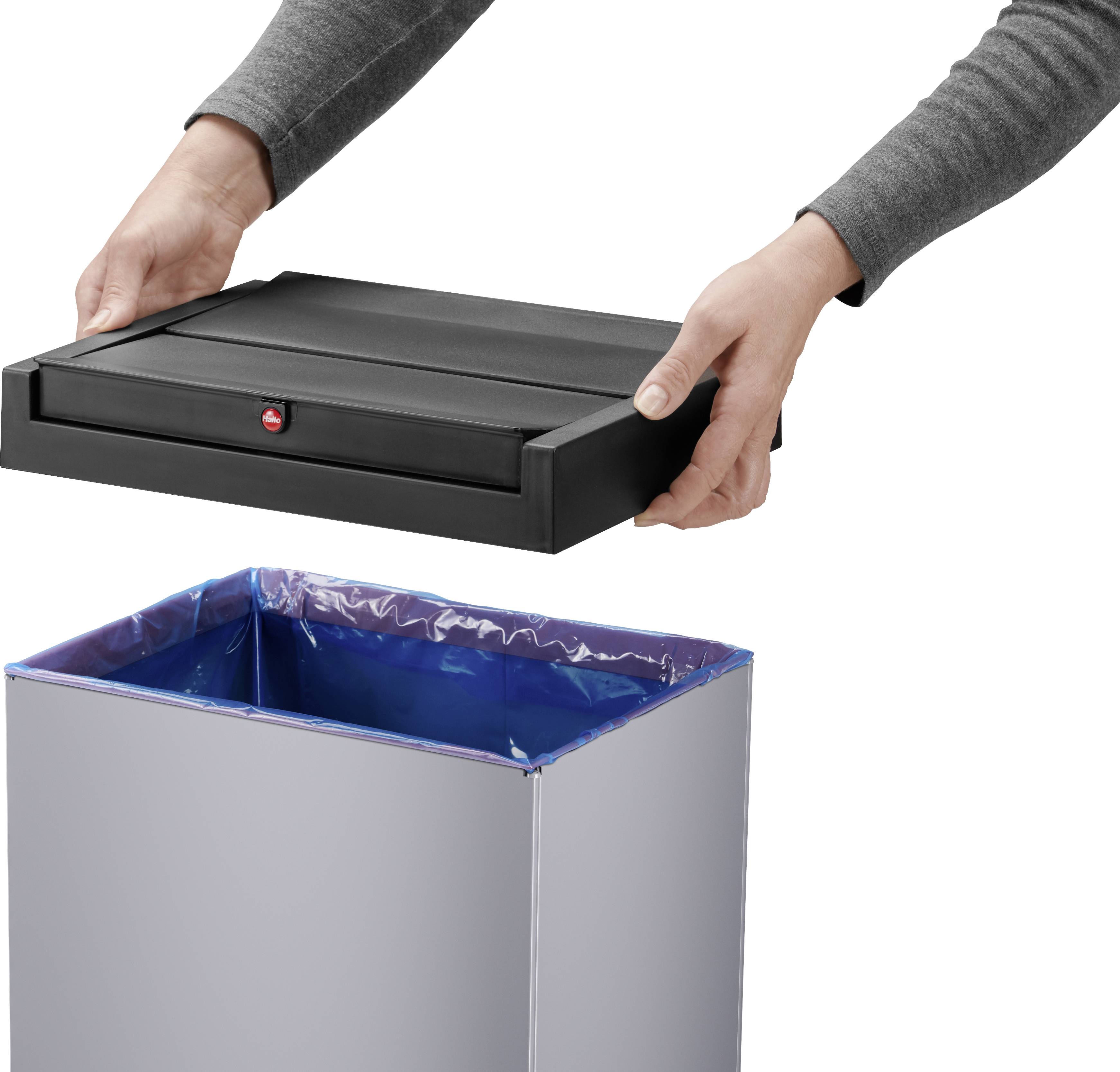 Osoba ostrożnie nakłada czarną pokrywę na szary kosz na śmieci z niebieskim workiem. Pokrywa ma czerwony przycisk.