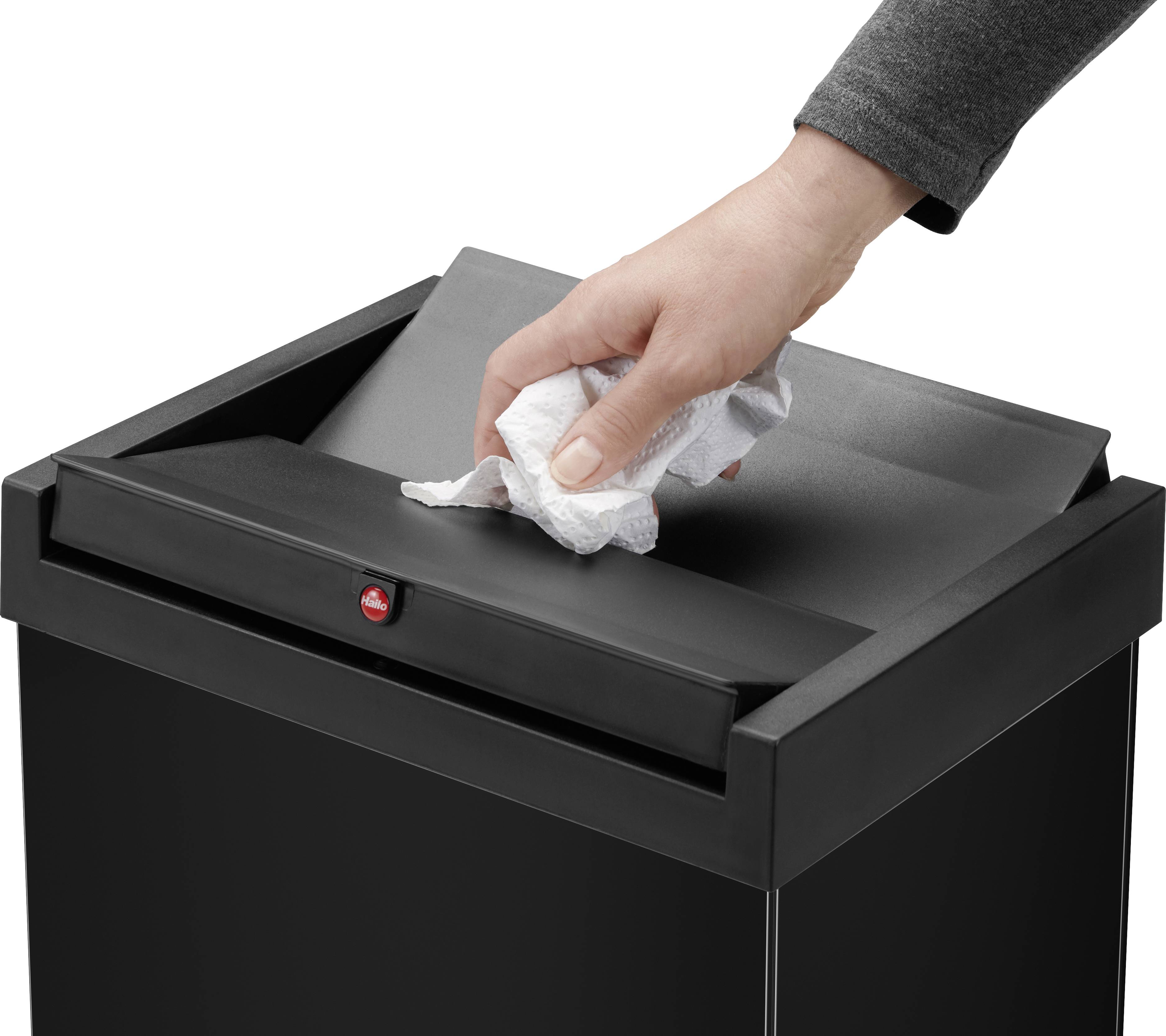 Ręka wrzuca zmięty papier do czarnego kosza na śmieci z klapą uchylną.