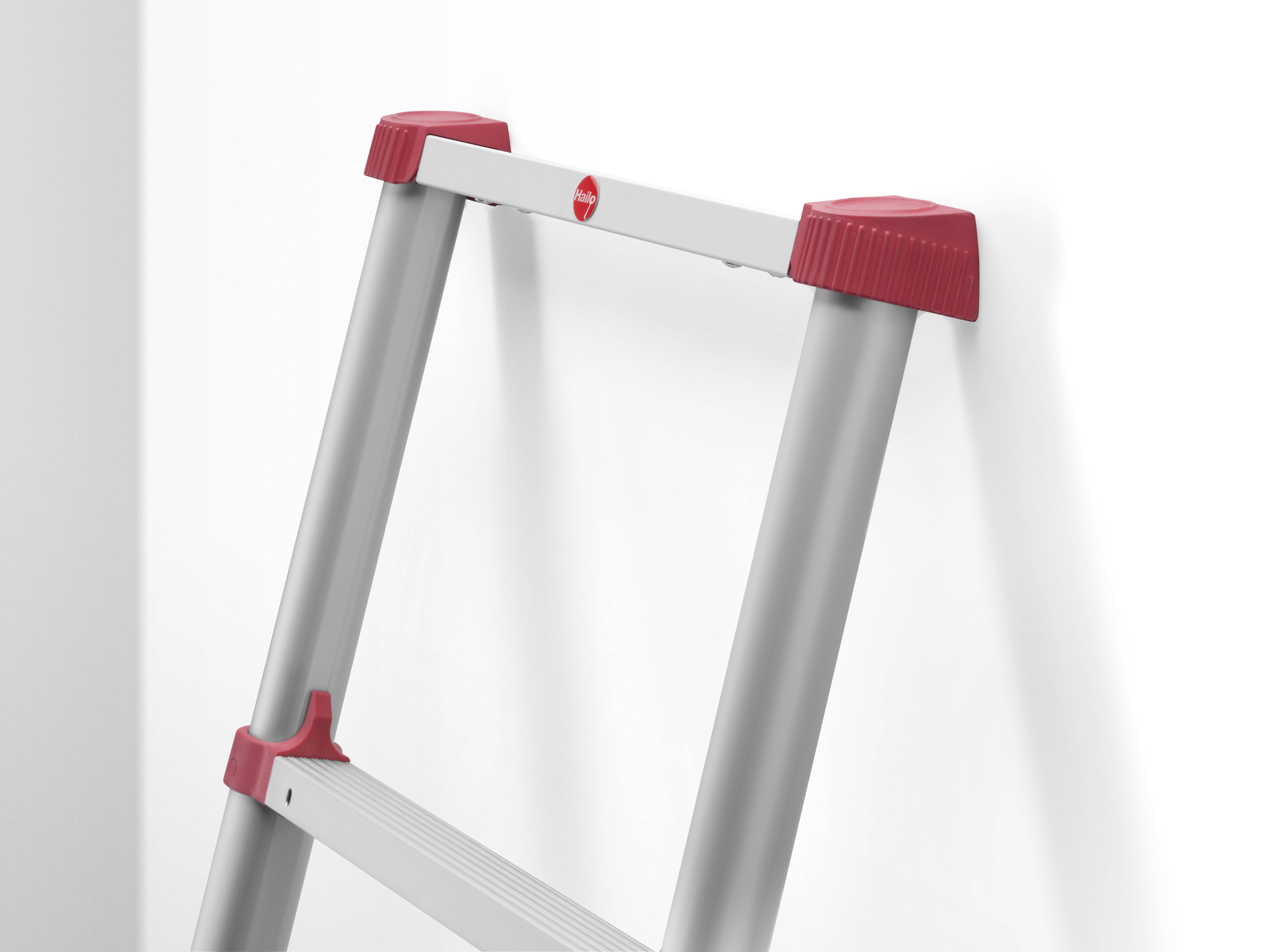 Szara drabina z czerwonymi stopkami stabilnie opiera się o białą ścianę.