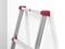 Szara drabina z czerwonymi nasadkami na końcach opiera się stabilnie o białą ścianę. Idealna do prac malarskich lub dostępu do wyższych partii.