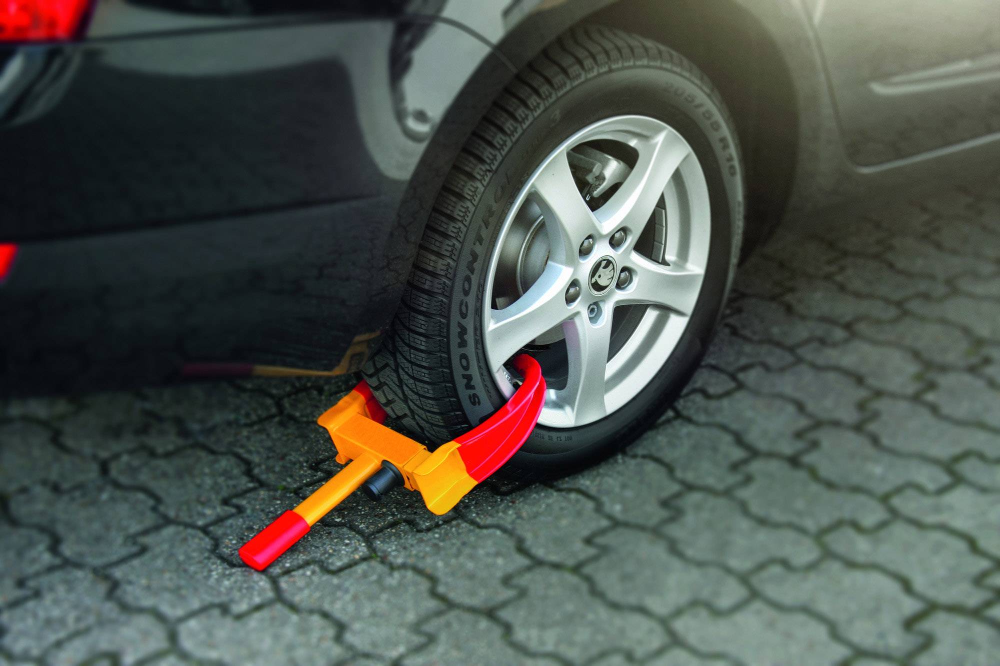 Opona samochodu jest zabezpieczona pomarańczową blokadą koła na wybrukowanej ulicy, aby zapobiec kradzieży lub przemieszczeniu.