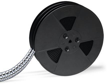 Duża czarna szpula z nawiniętą błyszczącą taśmą, przypominającą rolki filmowe, leży na powierzchni.