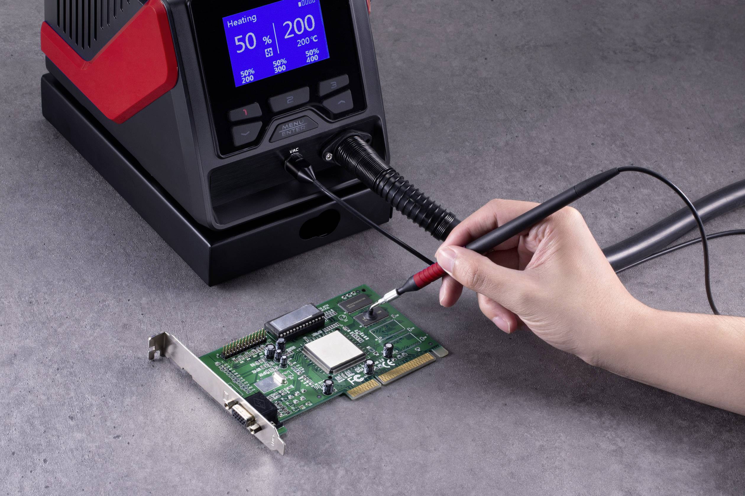 Osoba lutuje lutownicą na płytce drukowanej, trzymaną przez rękę. Stacja lutownicza wyświetla wskazania temperatury na wyświetlaczu.