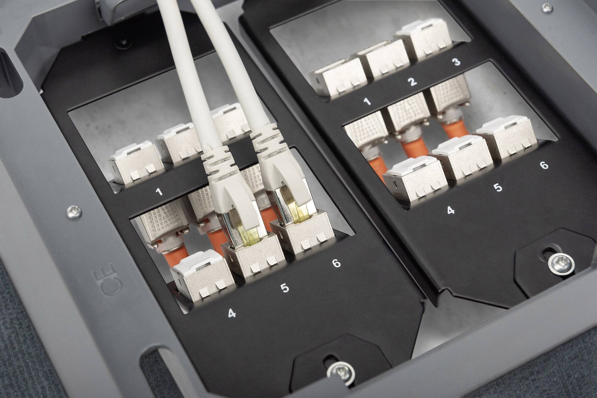 Dwa kable sieciowe są podłączone do portów w szarej szafce dystrybucyjnej, numerowanych od 1 do 6.