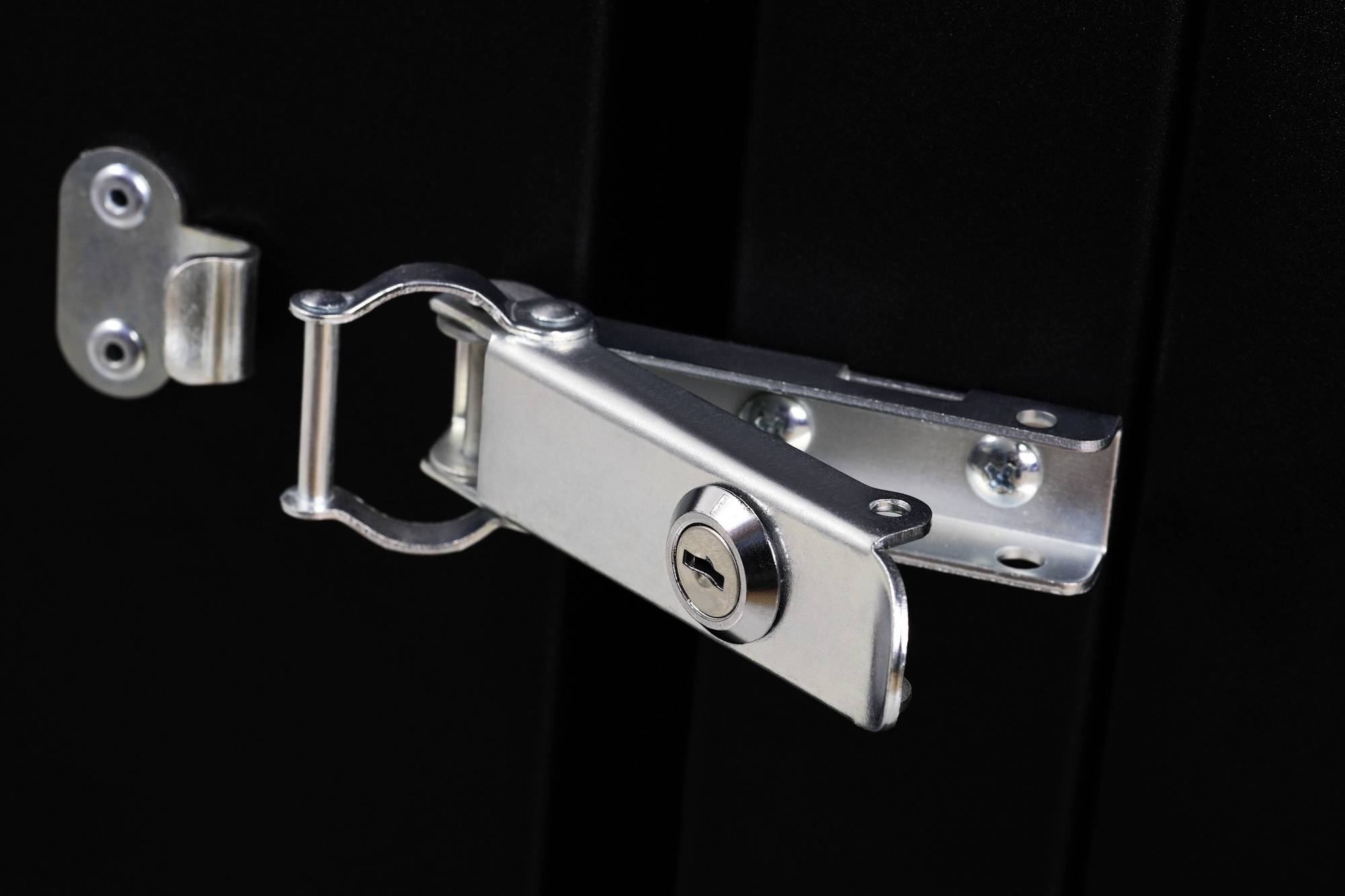 Metalowy zamek trzyma zamknięte ciemne drzwi. Klucz tkwi w zamku.