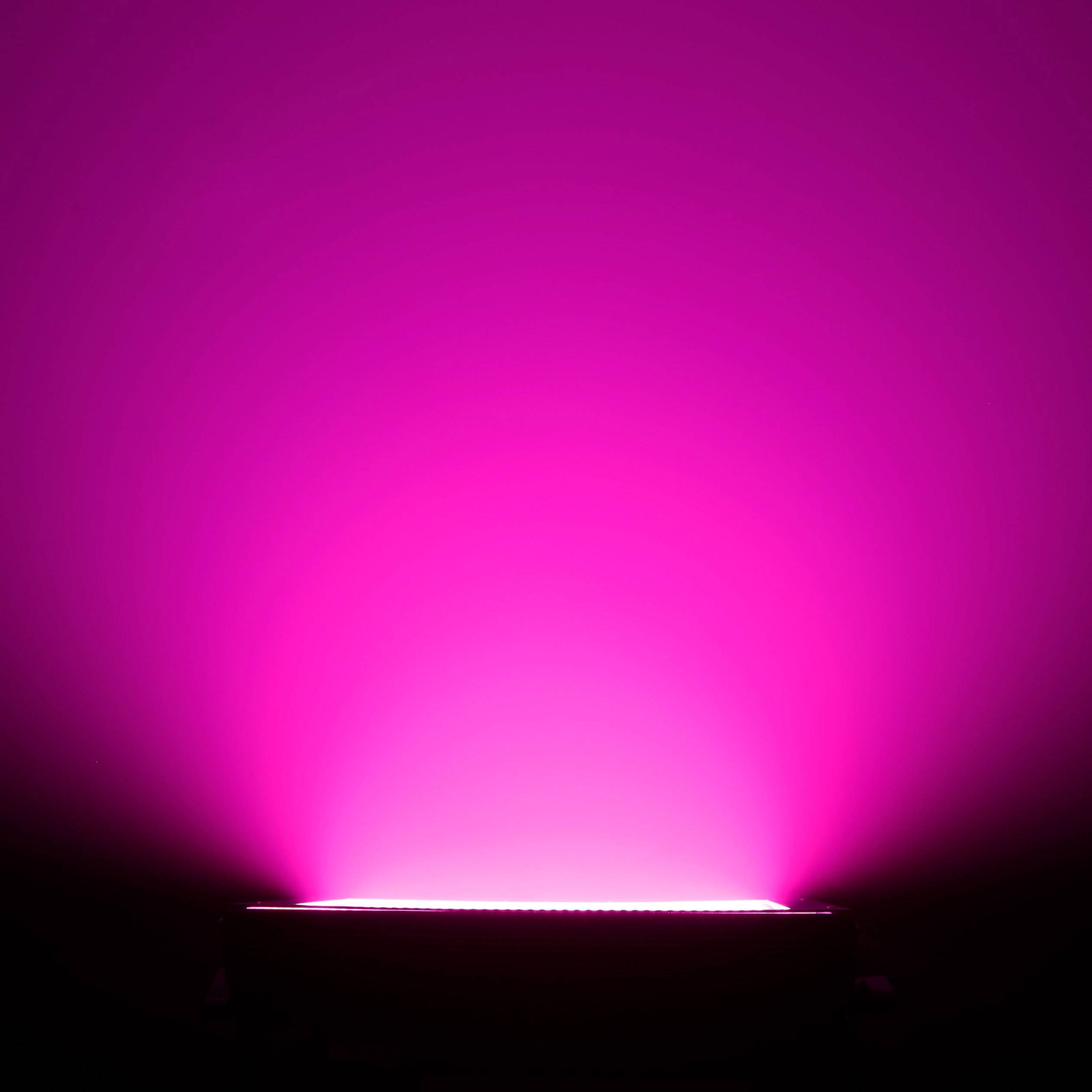 Jasne, różowe źródło światła emituje blask ku górze na czarnym tle, tworząc nastrojowe oświetlenie.