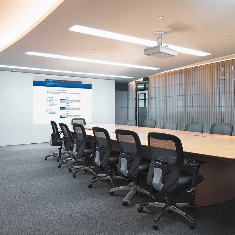 Nowoczesna sala konferencyjna z długim stołem i kilkoma krzesłami biurowymi. Na ścianie wyświetlana jest prezentacja.