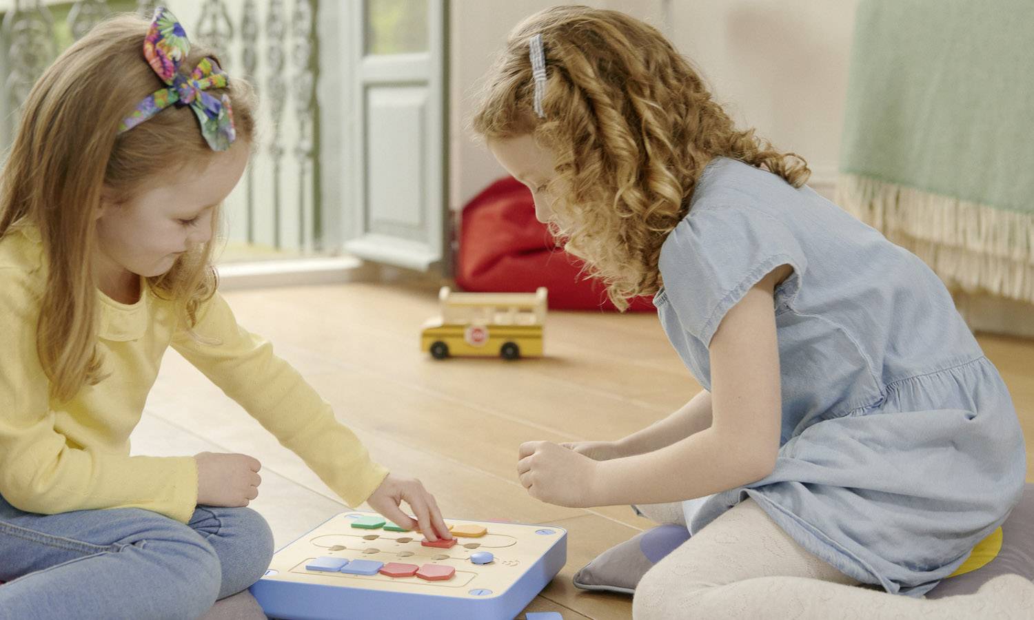 Dwie dziewczynki bawią się na podłodze drewnianą układanką. Wykazują się skupieniem i radością w jasnym, przytulnym pokoju.