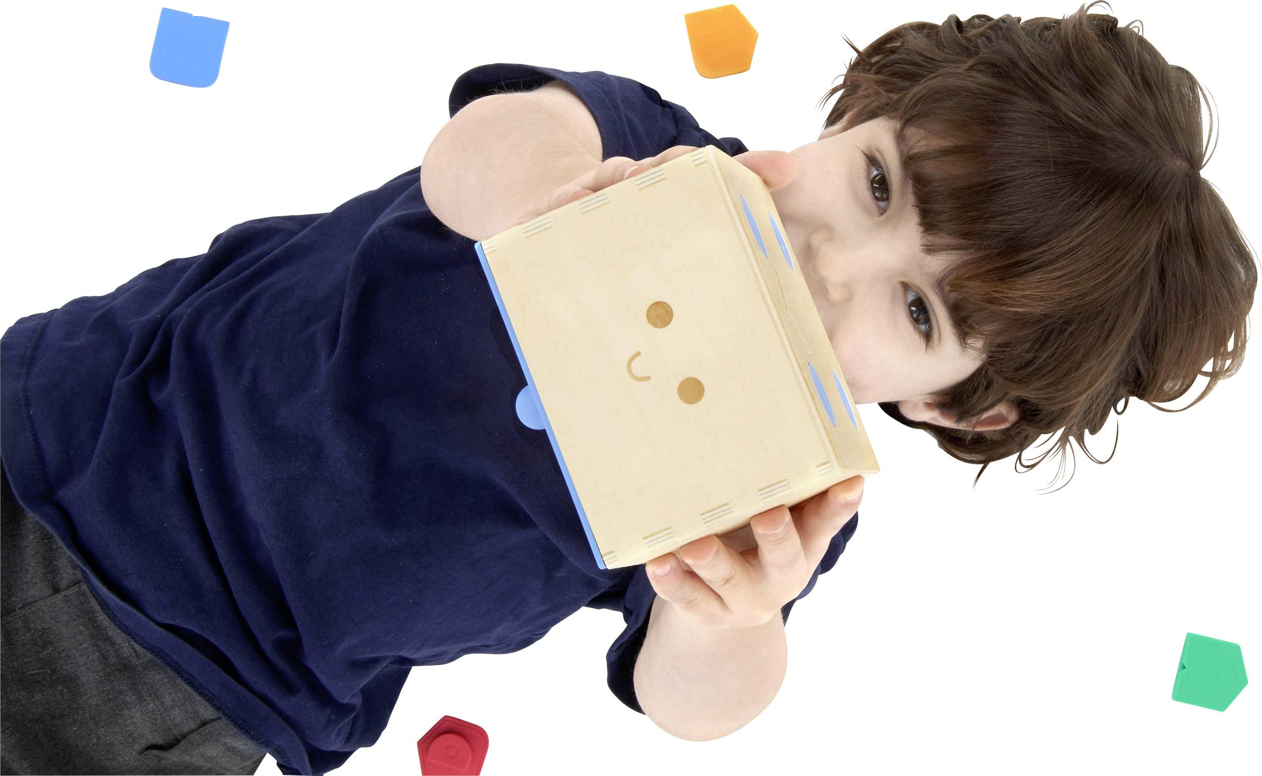 Dziecko trzyma sześcienny robot i się uśmiecha. Wokół dziecka rozłożone są kolorowe figury geometryczne.