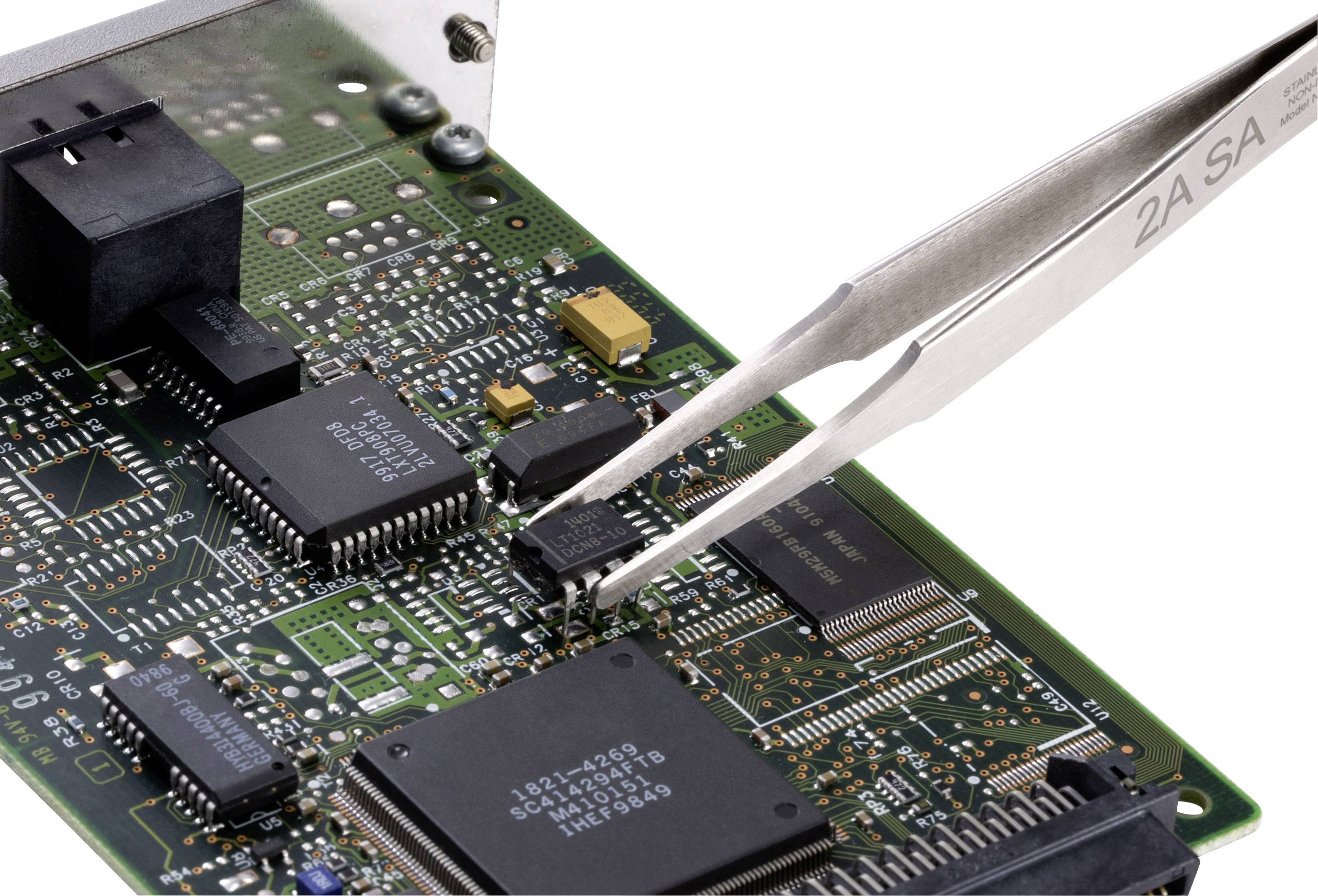 Pinceta trzyma mały, czarny chip ponad zieloną płytką drukowaną z licznymi elementami elektronicznymi.