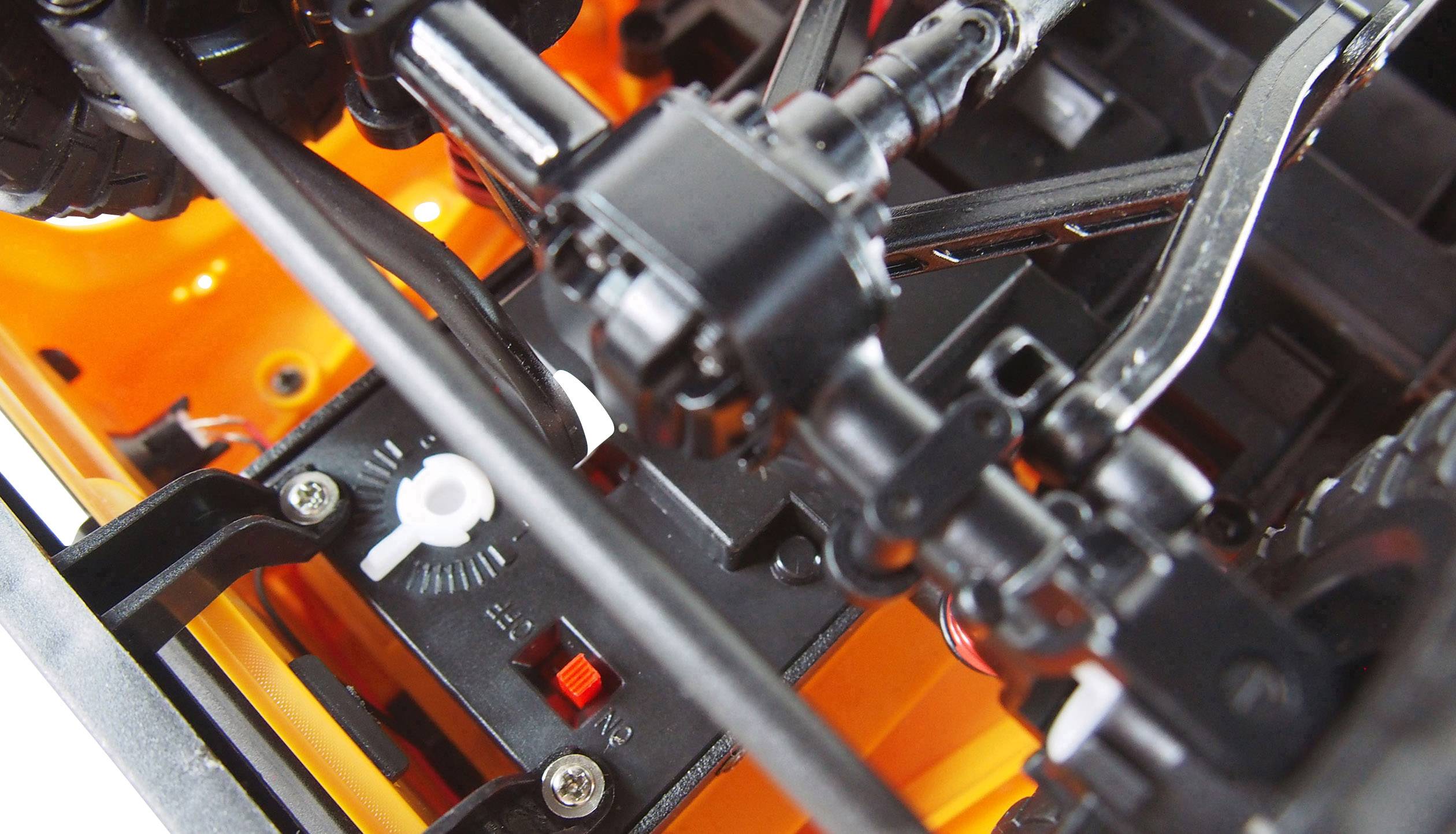 Zbliżenie modelu podwozia pojazdu z widocznymi elementami zawieszenia, śrubami i kołami zębatymi na pomarańczowym tle.