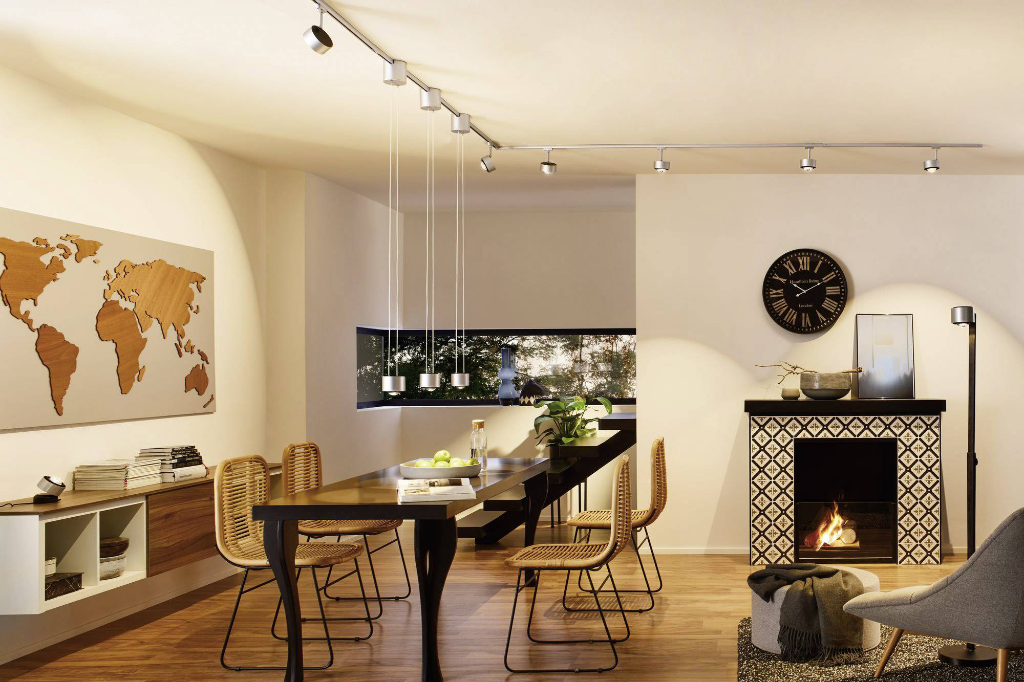 Przytulny obszar jadalny z drewnianym stołem i krzesłami, mapą świata na ścianie, kominkiem oraz oknami z widokiem na zewnątrz.