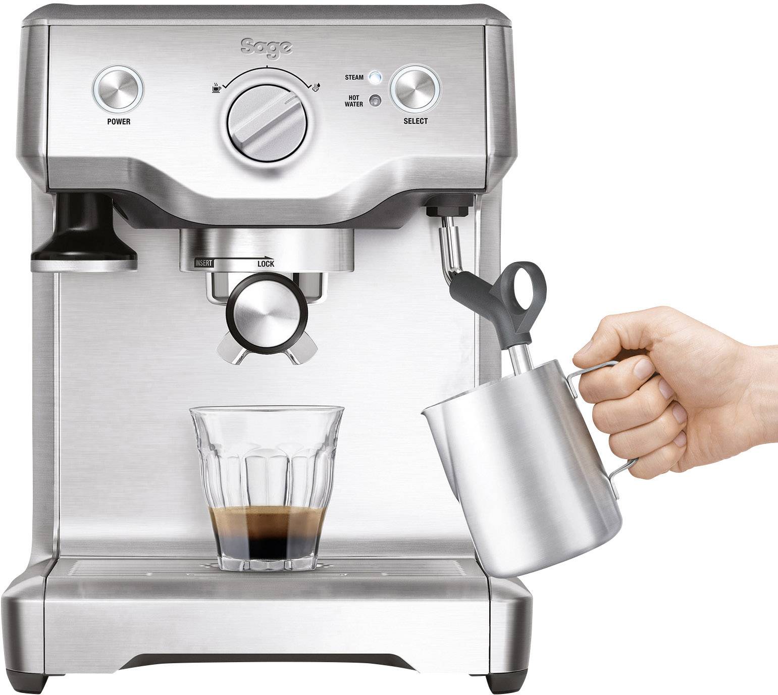 Srebrny ekspres do espresso, w którym jedna ręka trzyma dzbanek na mleko pod wylotem pary. Pod spodem stoi szklanka espresso.