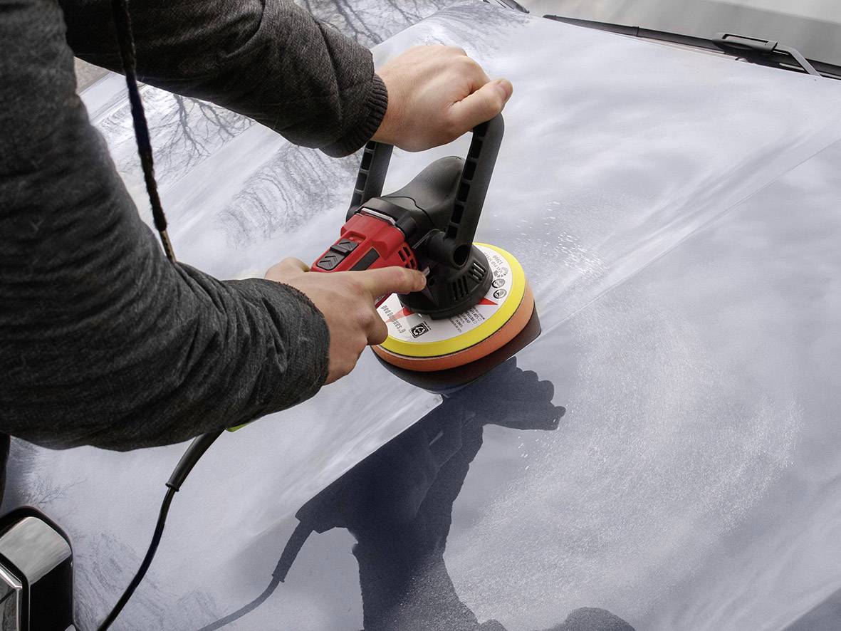 Jedna osoba poleruje lakierowaną powierzchnię samochodu elektryczną maszyną polerską.