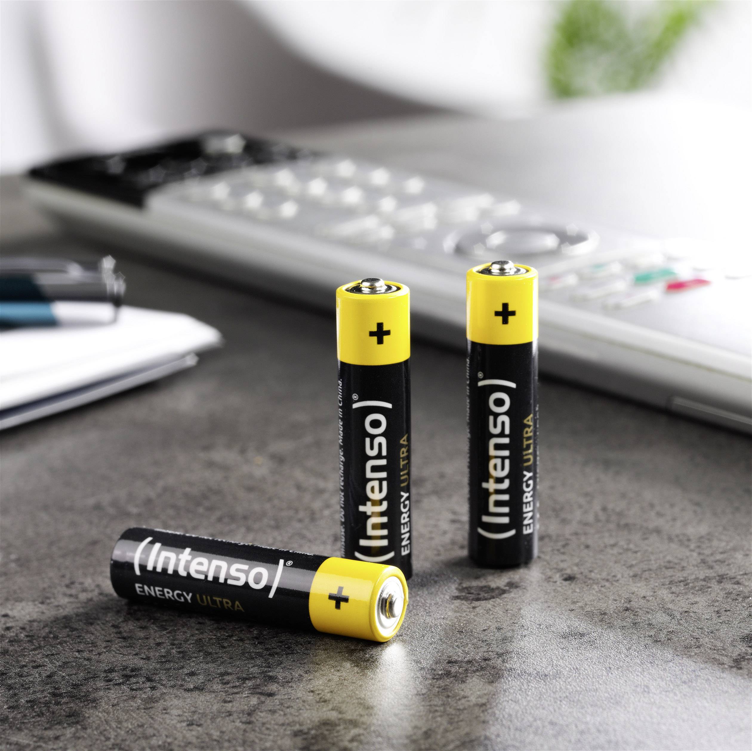 Trzy czarne baterie AA z żółtą górną częścią z napisem 'Intenso Energy Ultra' stoją na stole obok kalkulatora.