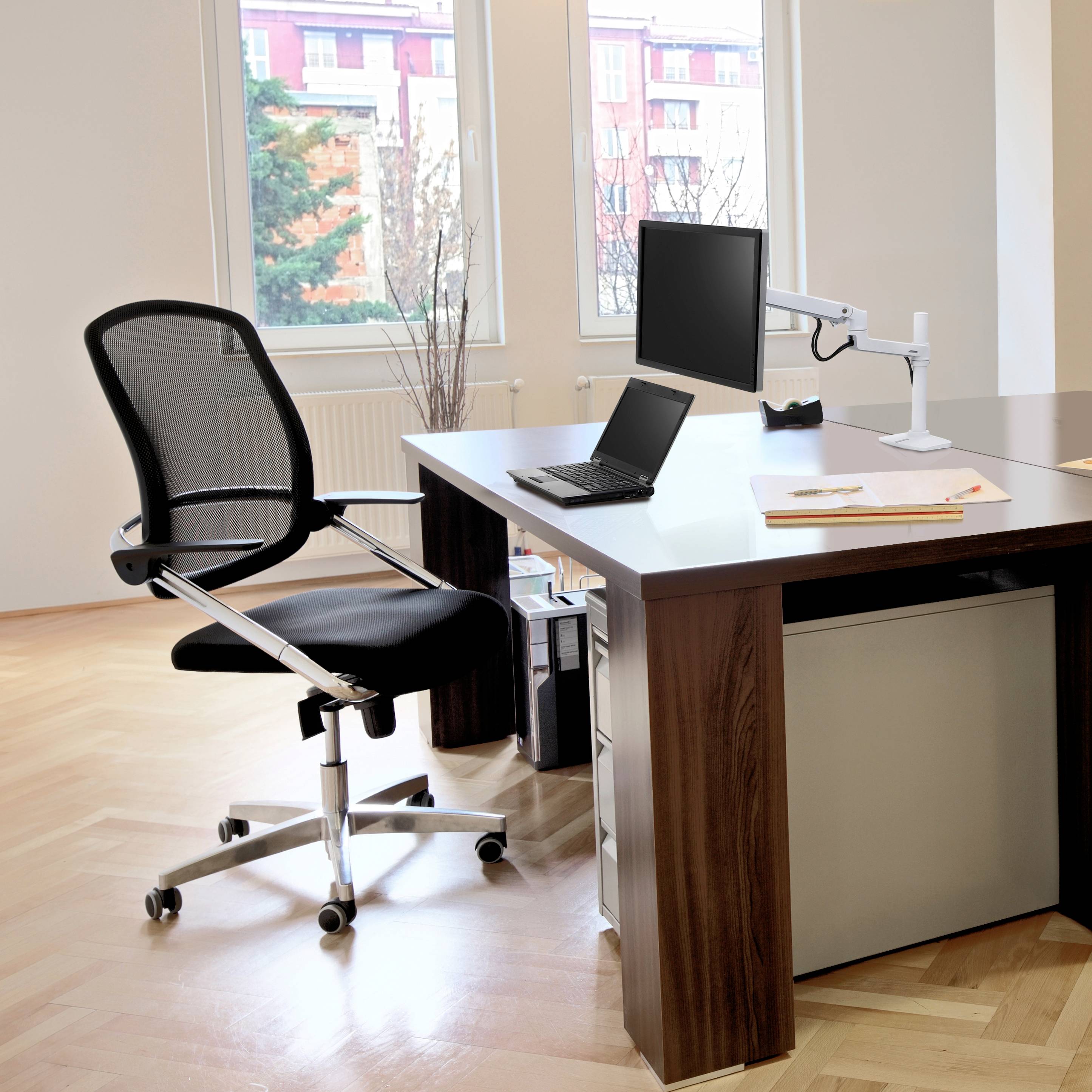 Nowoczesne biuro z drewnianą podłogą, biurkiem, laptopem i ergonomicznym krzesłem. Duże okna w tle zapewniają jasne światło.