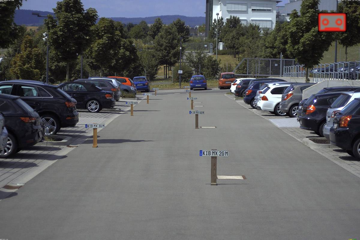 Duży parking z zaparkowanymi samochodami po obu stronach. Pośrodku znajdują się ponumerowane słupki wyznaczające miejsca parkingowe.