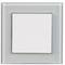 Kwadratowy, biały włącznik światła na kwadratowej, szklanej osłonie, na neutralnym tle.