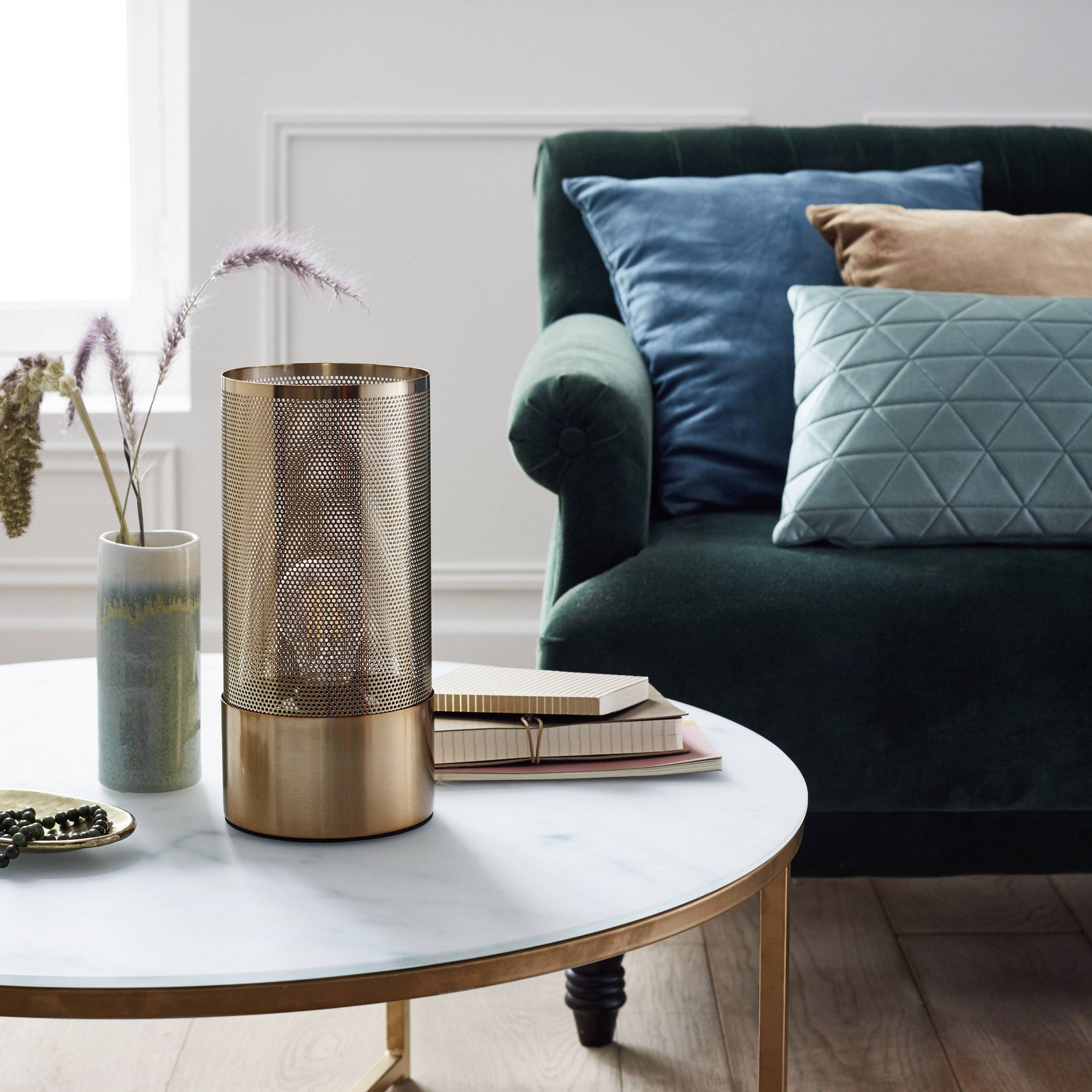 Stylowo urządony salon z zieloną sofą, dekoracyjnymi poduszkami oraz okrągłym stoliczkiem marmurowym ozdobiony elementami dekoracyjnymi.