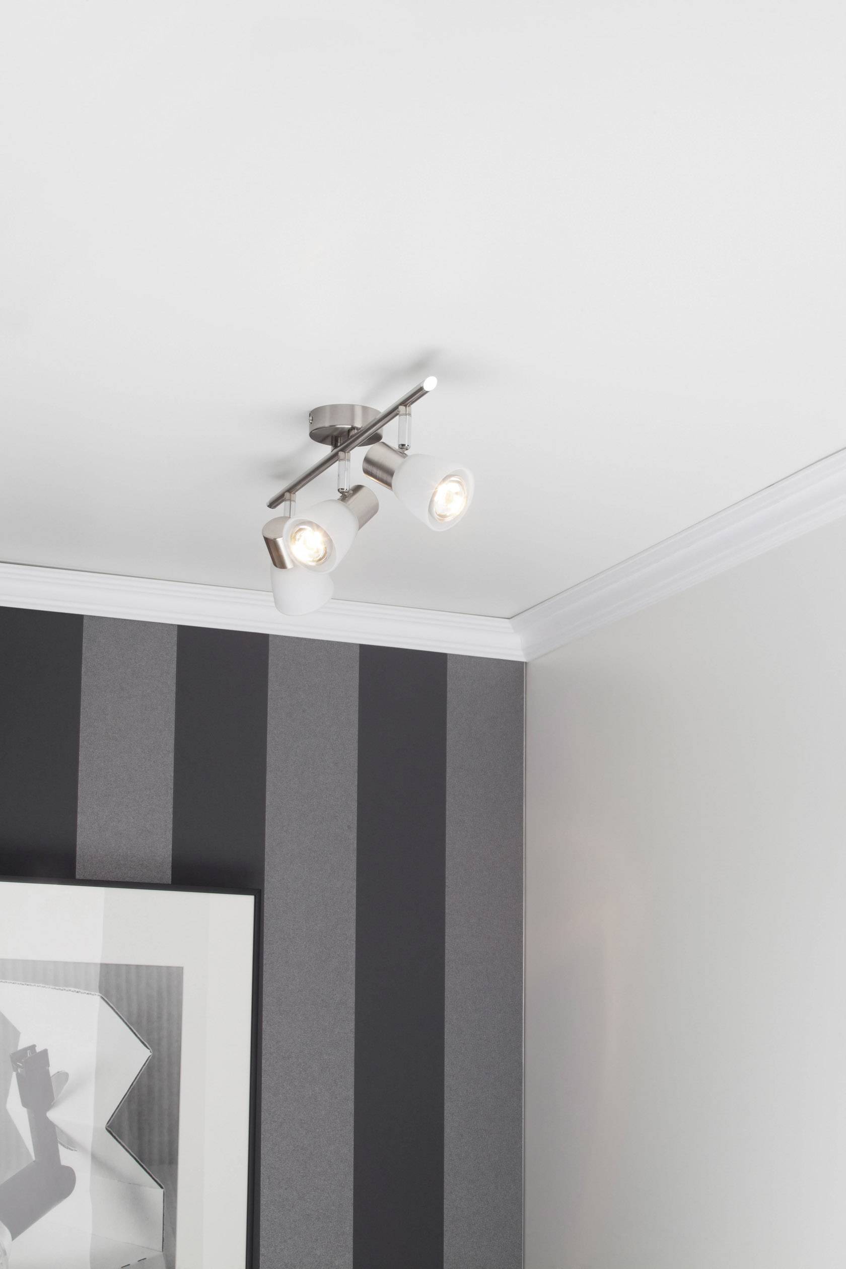 Lampa sufitowa z dwoma regulowanymi białymi reflektorami zamontowana na suficie nowoczesnego pokoju o ścianach w paski.