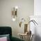 Lampa ścienna w stylu retro z dwoma okrągłymi żarówkami, umieszczona obok zielonej kanapy i złotego wazonu na małym stoliku. Atmosfera salonu.
