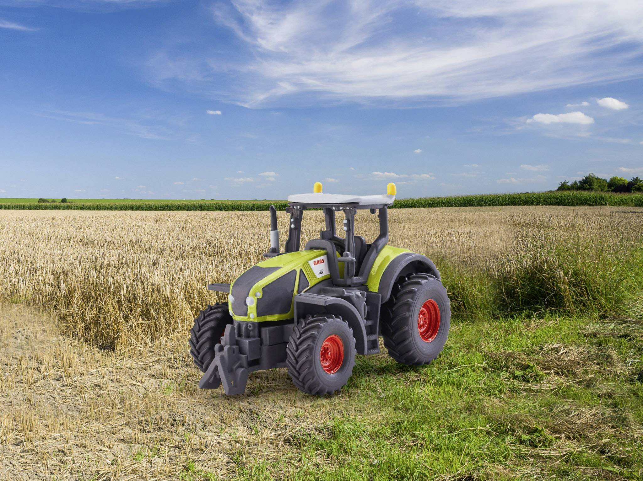 Zabawkowy traktor stoi na polu złotego zboża pod błękitnym niebem.