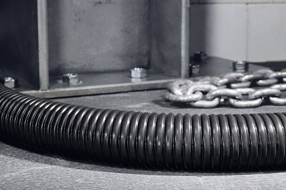 Czarny falisty wąż z tworzywa sztucznego leży na podłodze, obok metalowego łańcucha i stalowych elementów konstrukcyjnych.