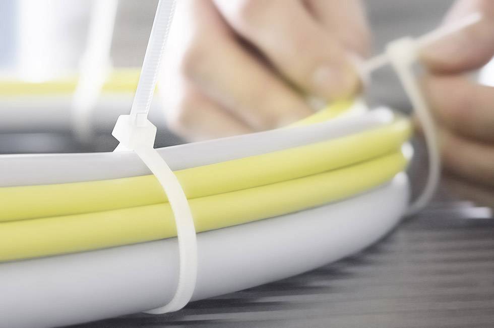 Zbliżenie na dwie ręce wiążące żółte i białe kable białą opaską zaciskową.