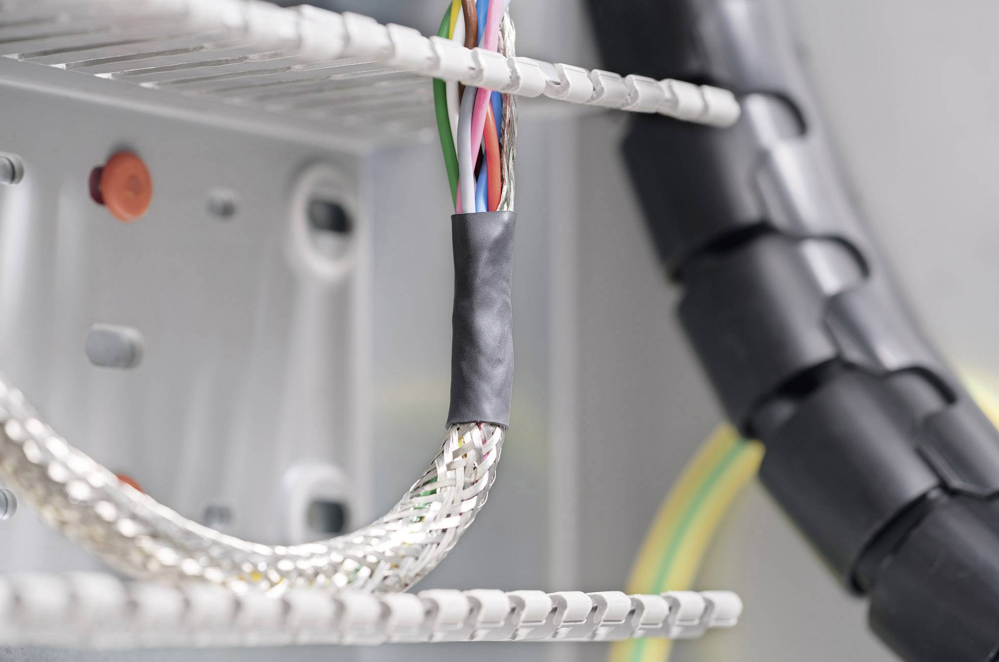 Wiązka przewodów elektrycznych jest ułożona w sposób uporządkowany w szafce rozdzielczej. Niektóre kable są otulone czarną gumą.