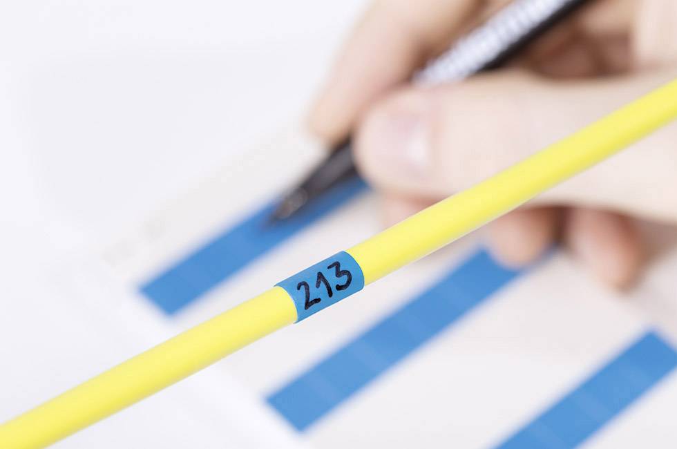 Osoba trzyma żółty marker z numerem 213, a w tle widać rozmyte niebieskie wykresy słupkowe na papierze.