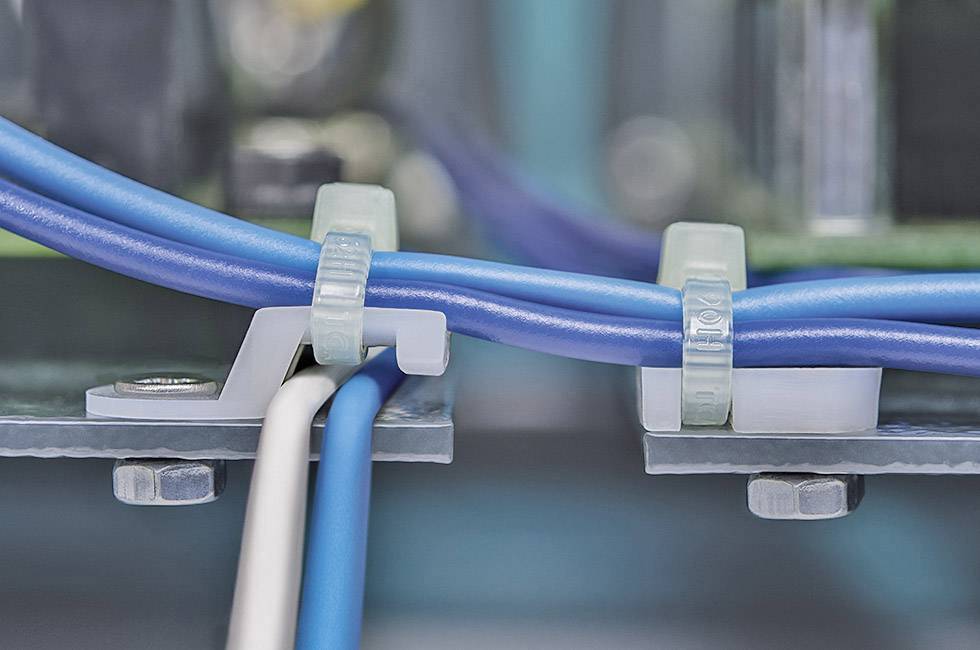 Zbliżenie niebieskich i białych przewodów przymocowanych opaskami kablowymi do metalowej płyty. W tle widoczne są nieostre kable.