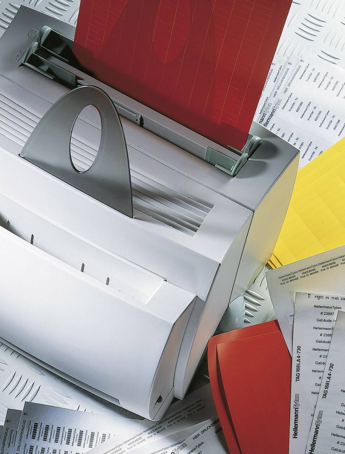 Drukarka z czerwonymi i żółtymi kartkami, otoczona dokumentami na stole.