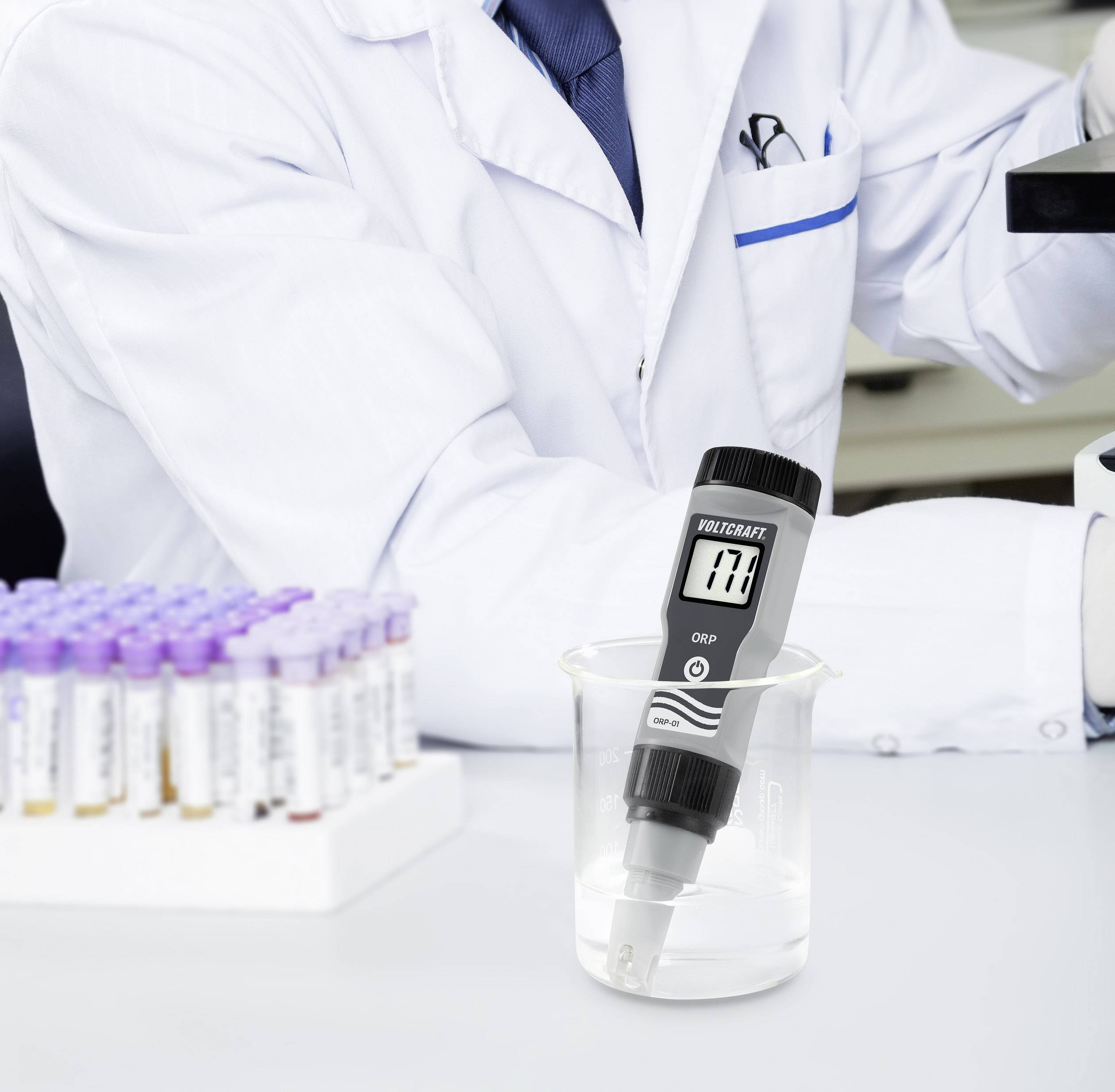 Naukowiec w białym kitlu mierzy pH płynu w zlewce za pomocą cyfrowego pH-metru.