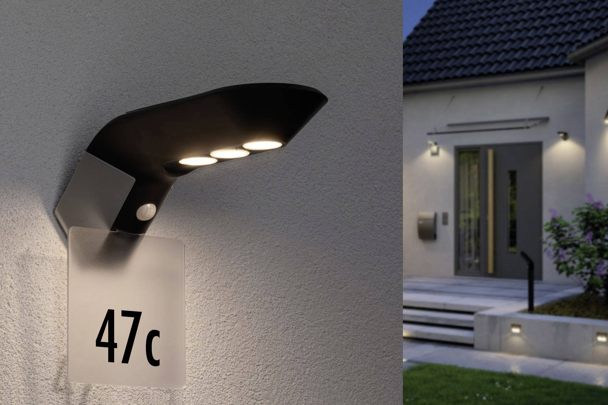 Lampa zewnętrzna z numerem domu '47c' na ścianie. W tle nowoczesny dom o zmierzchu z dekoracyjnym oświetleniem.