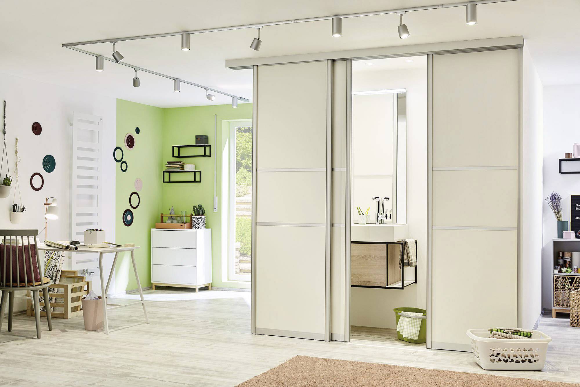 Jasny salon z biurkiem, regałami i przesuwnymi drzwiami zakrywającymi łazienkę. Nowoczesne wnętrze utrzymane w zieleni i kolorach ziemi.