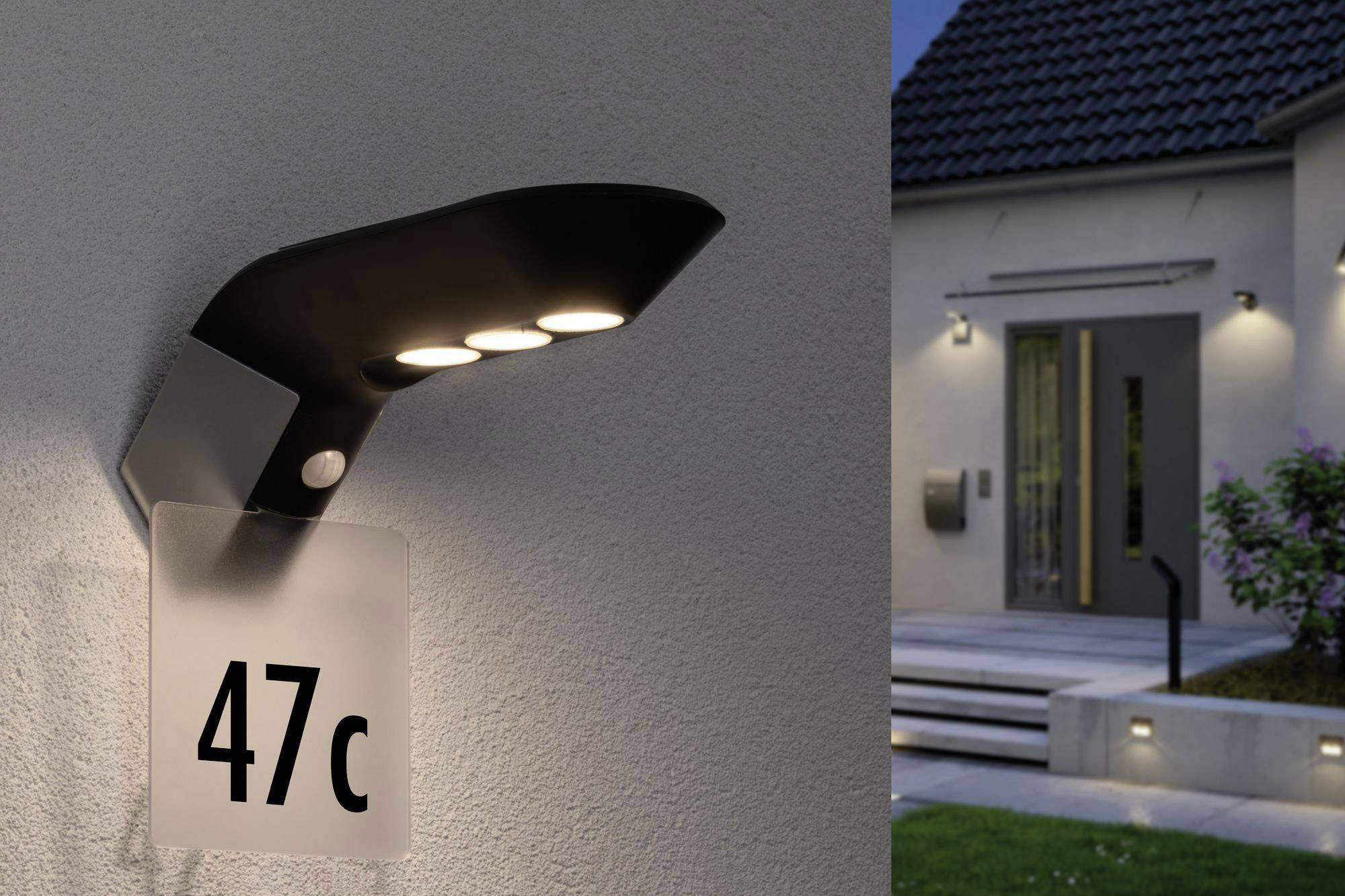 Widok z zewnątrz nowoczesnego domu nocą z oświetlonym budynkiem i reprezentacyjnym numerem domu '47c' przy oświetlonej lampie ściennej.