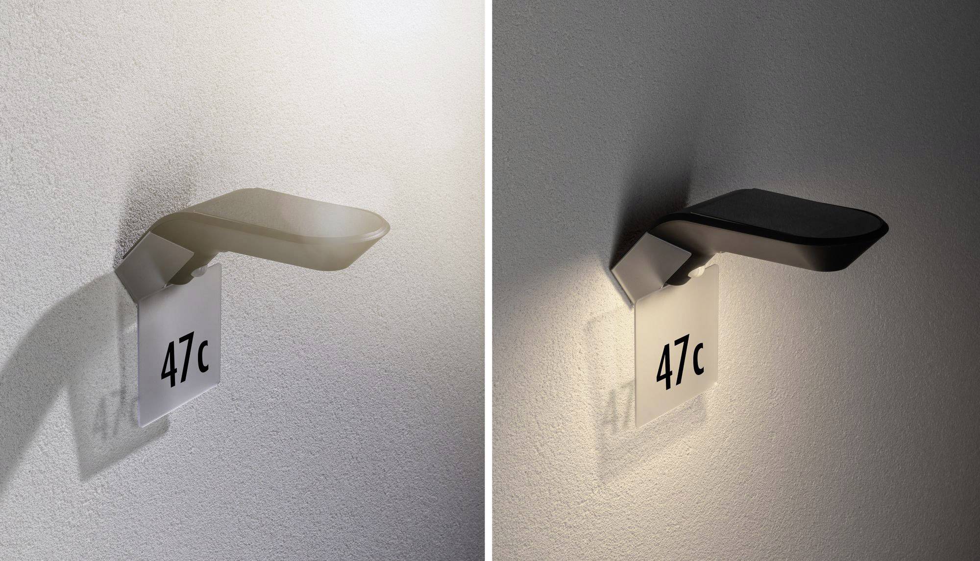 Uchwyt na tabliczkę w kolorze srebrnym z napisem '47c', zamocowany na ścianie i oświetlony lampą.