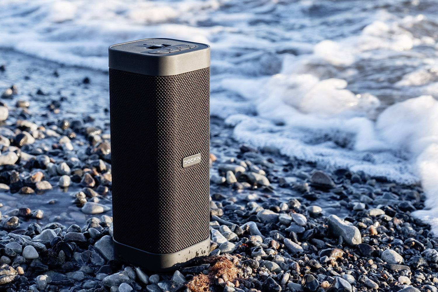 Przenośny głośnik umieszczony na żwirowej plaży, w pobliżu morskich fal.