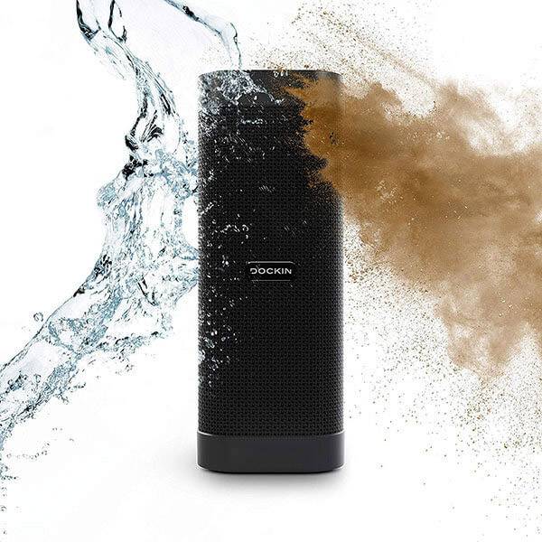 Przenośny, cylindryczny głośnik jest spryskiwany wodą i piaskiem, co demonstruje jego wytrzymałość i odporność na warunki atmosferyczne.